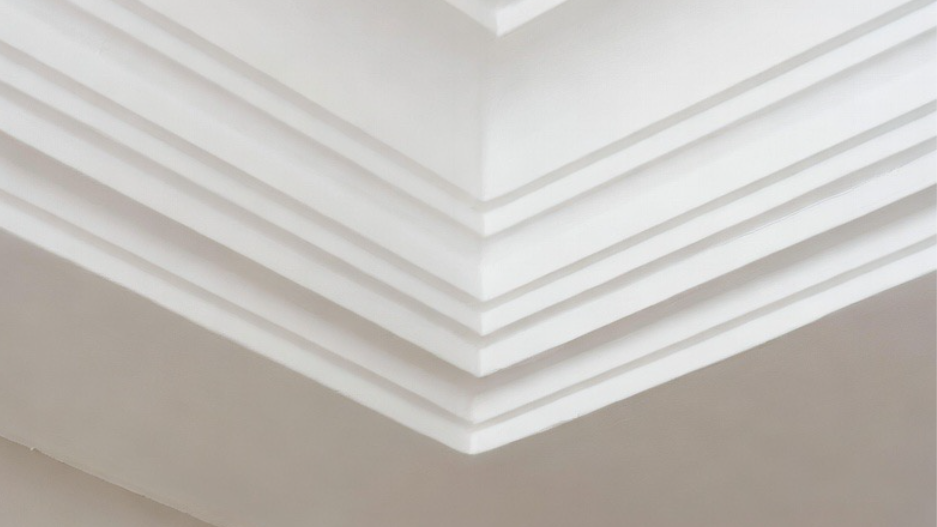 Close-up of a ceiling with white crown molding and recessed lighting.